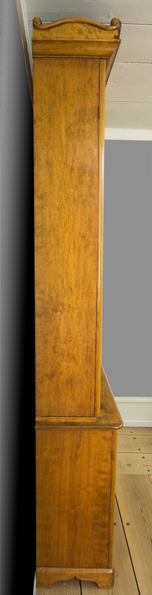 Skåp tillverkat i furu och björk. Möbeln består av två delar, upptill en vitrindel med hyllor och nedtill en del med skåp. Vitrindelens dörrar är glasade med spröjsverk. Den övre delen avslutas upptill med ett krön. Krönet är dekorerat med trädekorationer formade som voluter. Skåpdelen nedtill har dörrar med speglar.