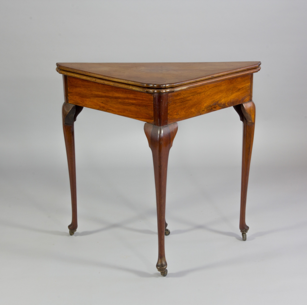 Spelbord, trekantigt med svängda ben. I uppfällt läge är bordet kvadratiskt, fällskivan stöds av ett ben som dras fram ur sargen. Två lådor med mässingsknappar. Skivans klädsel av grönt ylle. 

Klädseln av ett senare datum,  tidigt 1900-tal.