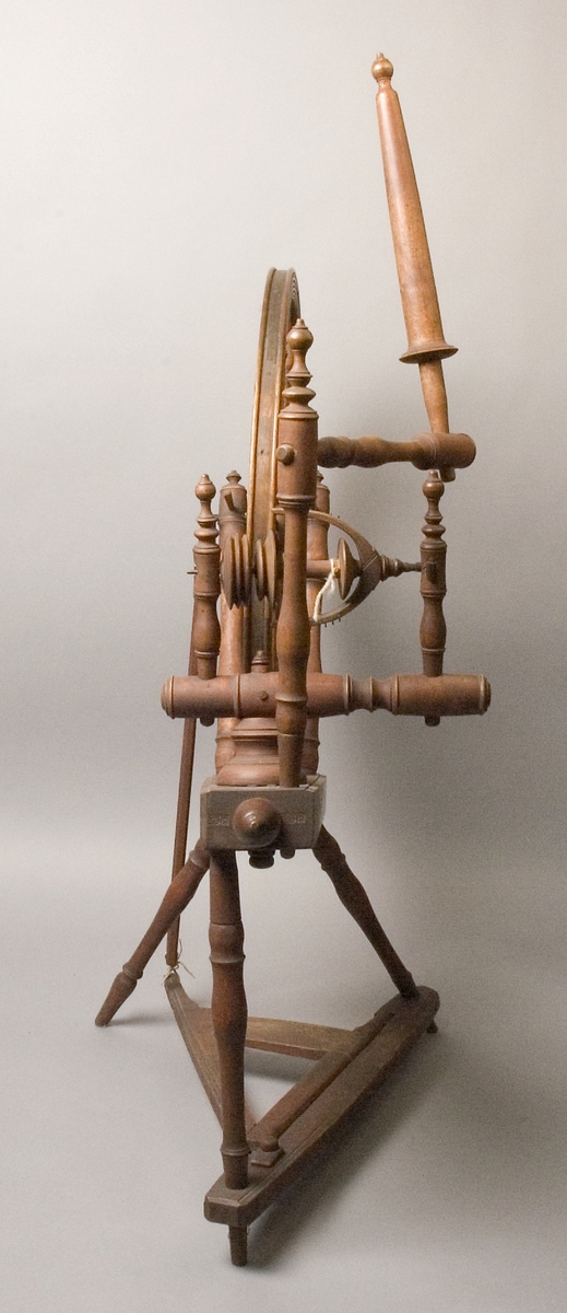 Spinnrock tillverkad av trä. Sedvanlig modell med lutande bord och tre ben. En extra spole, omärkt, hänger på rocken. Svarvade ben, ekrar, ståndare och linfäste.