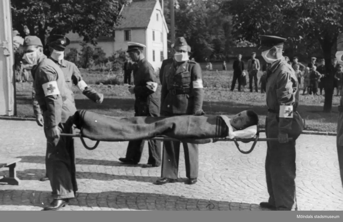 "Karantänsförläggning" på Kvarnbyskolan för överlevande från koncentrationsläger i Tyskland och Polen 1945.  
Skolan fungerade under denna sommar som beredsskapssjukhus.

Patient bärs in i förläggningen på bår av Röda Kors-arbetare.