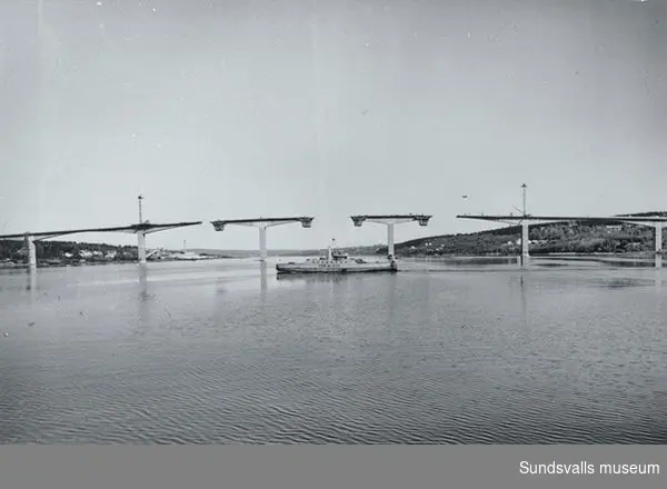 Alnöbron under byggnation och på vattnet trafikerar färjan 243 Alnösundet.