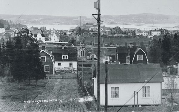 Stadsvy som visar västra Skönsberg med blandade bostadstyper och tillhörande tomter. I bakgrunden Ortviken och Sundsvallsfjärden. Vykort.