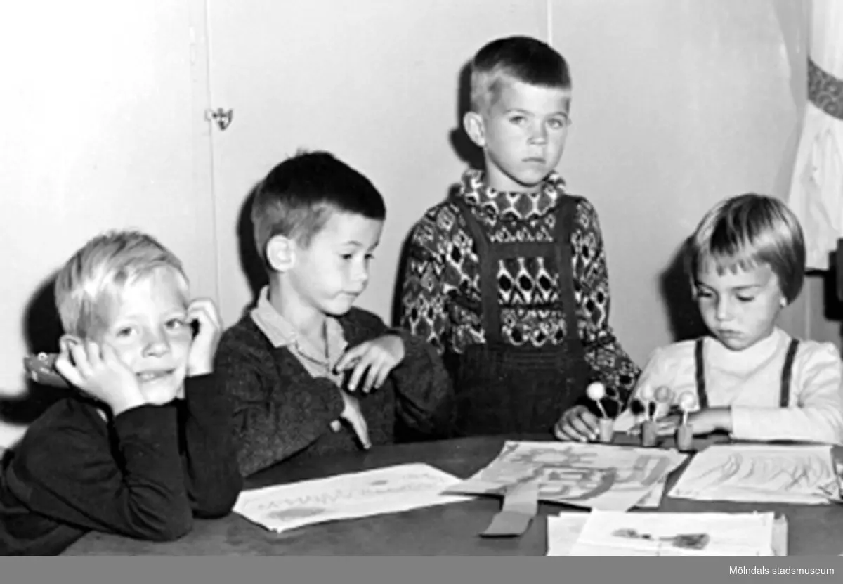 Fyra barn som sitter vid ett bord där det ligger målade teckningar. Holtermanska daghemmet 1953.