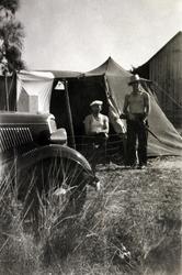 To menn foran et telt, karen til høyre med bar overkropp og 