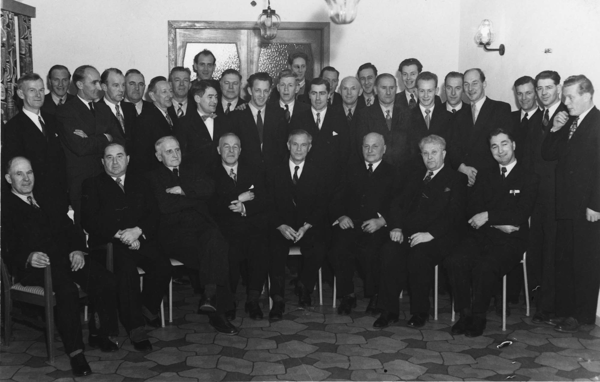 Gruppebilde av menn på invielsesfest hos HORB i forbindelse med de nybygde anleggene på Torvet og Sama, vinteren 1955-1956.