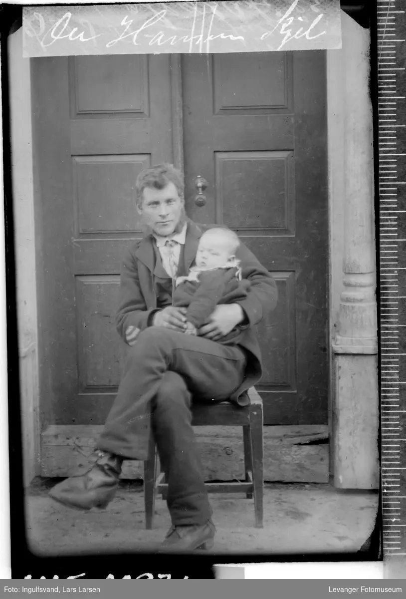 Portrett av en mann og et spedbarn foran et inngangsparti.