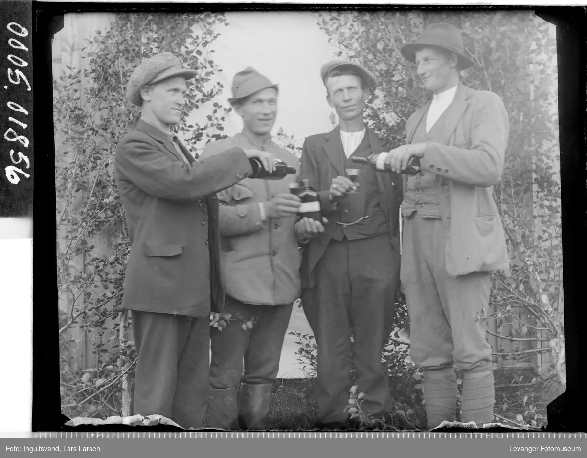 Gruppebilde av fire menn som har et drikkelag.