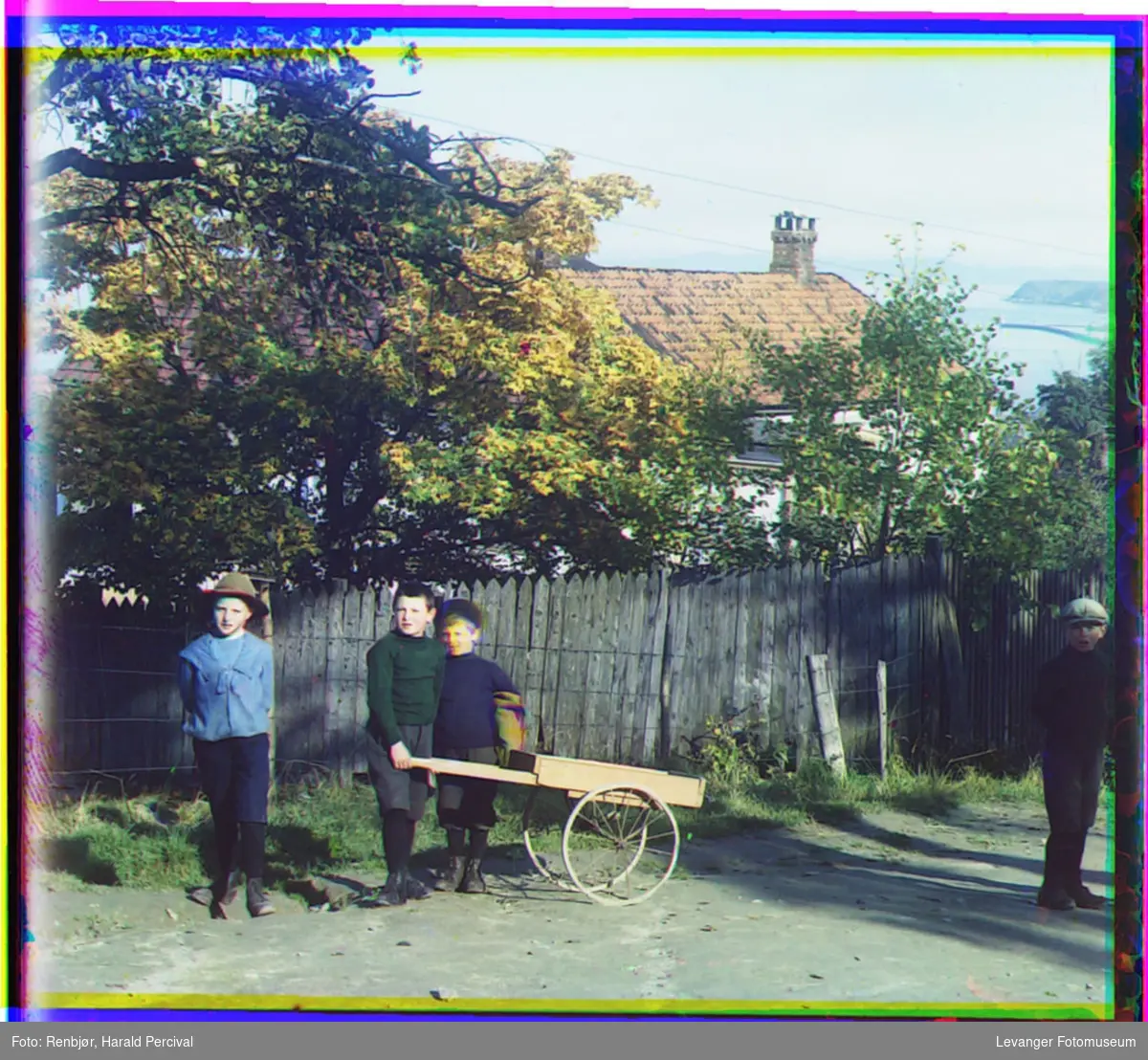 Fire gutter med håndkjerre foran en et hus med gjerde.