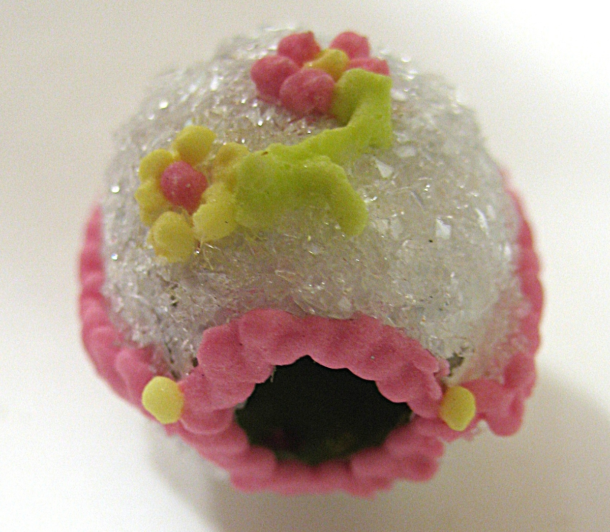 Litet tittägg tillverkat av socker. Ägget är vitt med rosa dekor runt öppning och sidor. På ovansidan finns två blommor. Inne i ägget finns en fågel i ett grönt landskap.
 

Ägget inköptes 1998 inför utställningen vårseder.