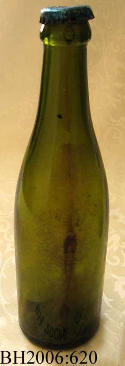 Ølflaske av grønt glass uten etikett, med orginal kork. Korken er blå.