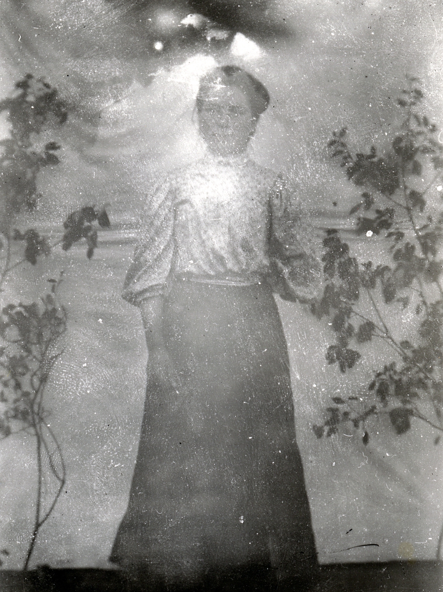 Kvinne i lys skjorte og mørkt skjørt, i helfigur foran lerret