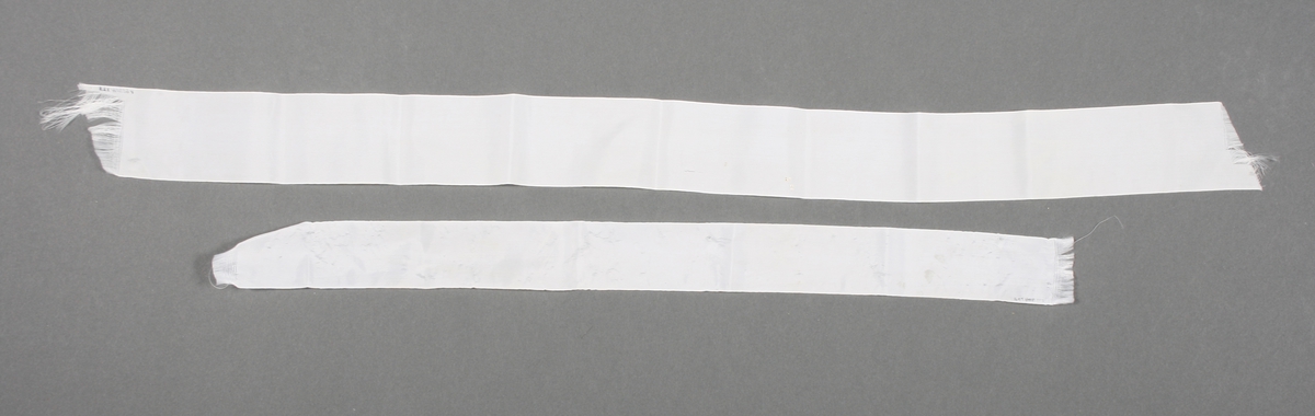 To hvite bånd brukt som hårsløyfer. Det er ulik bredde og lengde på dem, se "Mål". Båndene er av nylon.