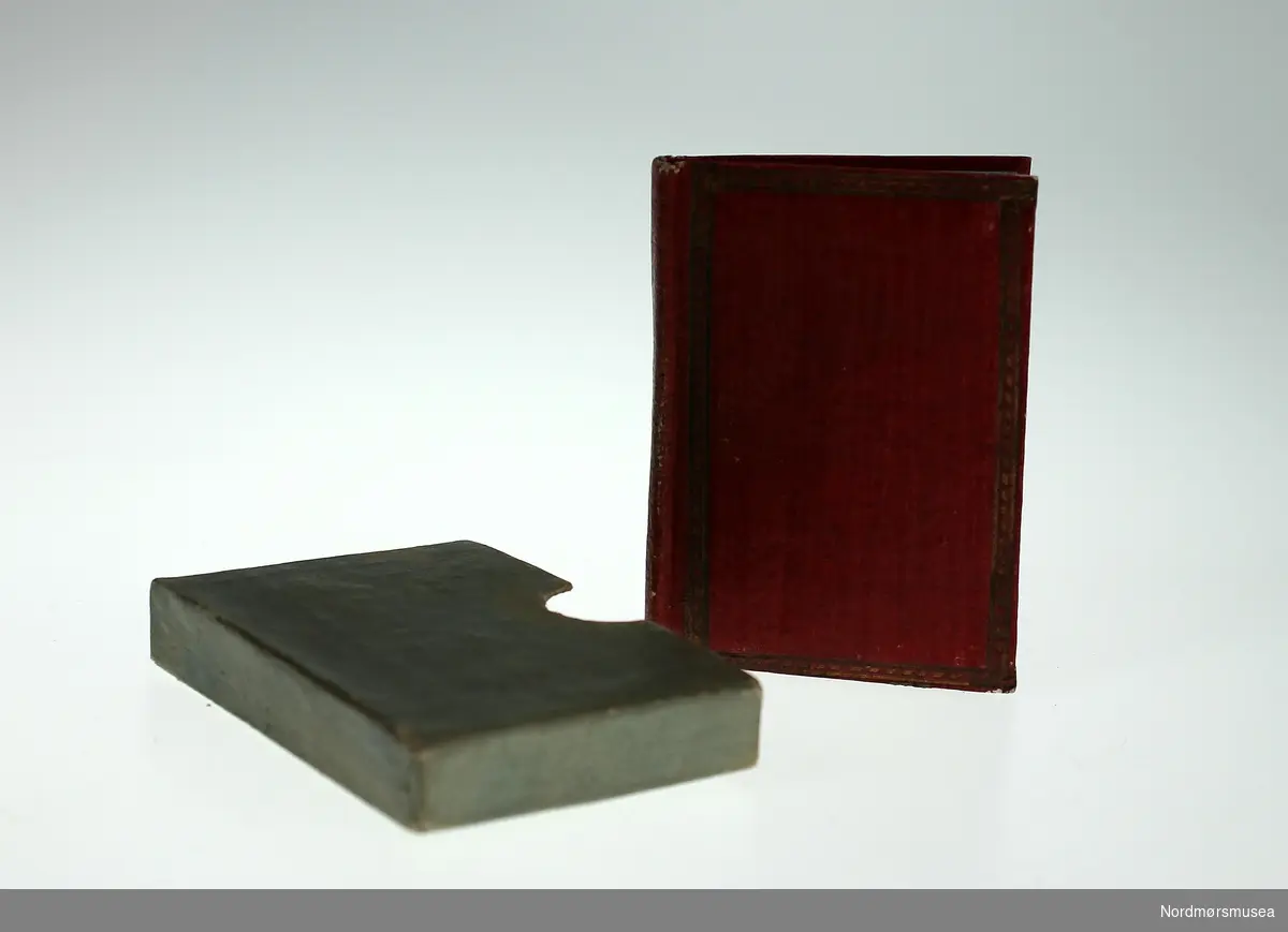 Bok i pappkassett med vareprøver av ullklede i tre farger (gul, brun og rød.)