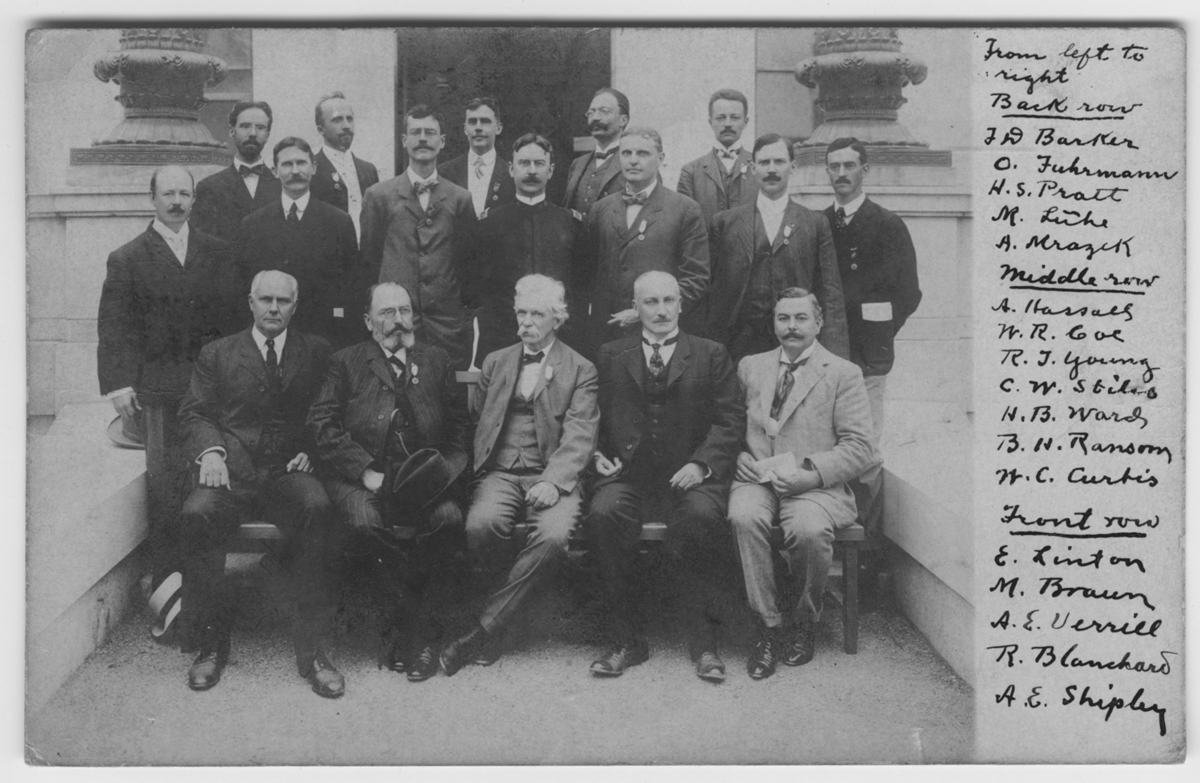 'Gruppbild med 17 män samlade utanför byggnad. Delatagare vid Internationella zoologkongressen i Boston 1907. Skickat som vykort till Leonard Axel Jägerskiöld från R. Blanchard, Albert Hassall m.fl. :: Från vänster till höger: :: Bakre raden: J. W. Barker, O. Fuhrmann, H. S. Pratt, M. Lühe, A. Mragck. :: Mittraden: A. Hassall, W. R. Goe/Coe, R.J. Young, C.W. Stiles, H.B. Ransom, W.C. Curtis. :: Främre raden: E. Linton?, M. Braun, A.e. Uevrill, R.B. Canchard, A.e. Shiphy.'