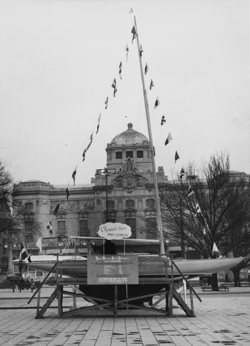 Fartyg: KSSS 1947                     Bredd över allt 1,95 meterLängd över allt 8,90 meterRederi: KSSSByggår: 1947Varv: Svensson & Dahlströms Båtvarv, KarlstadKonstruktör: Anker, JohanÖvrigt: KSSS lottbåt 1947 utställd i april på Nybroplan i Stockholm, med Berzelii park i bakgrunden. Båten tillföll vid utlottningen Lennart Sundqvist.