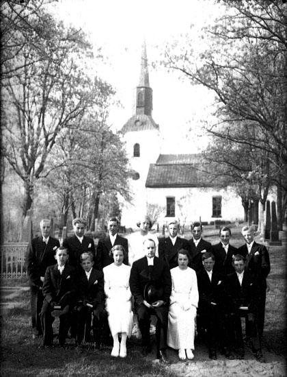 Konfirmander, 3 flickor, 11 pojkar och kyrkoherde Gösta Sköldebrand.
Kils kyrka i bakgrunden.