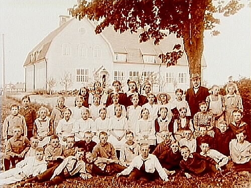 Almby skola, 46 skolbarn med lärare Gustaf Karlsson.
Skolbyggnaden i bakgrunden.