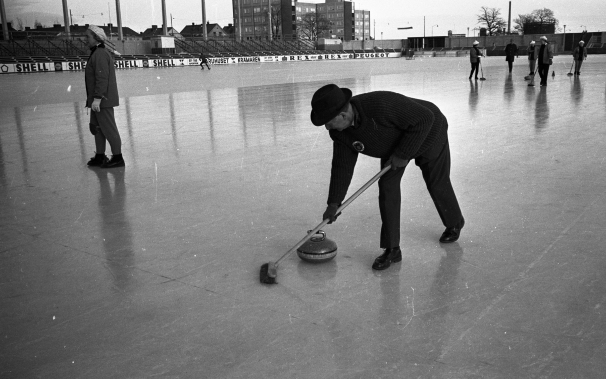 Curling på Vinterstadion, 11 februari 1965.

Åtta personer på bilden. En man i hatt spelar i förgrunden.
