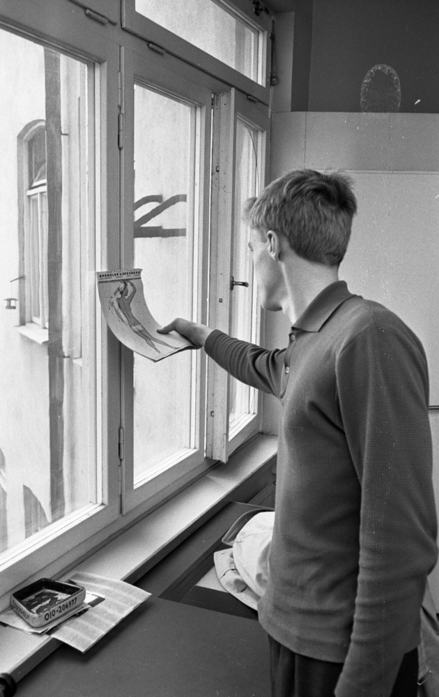 Beg. bilar, Ferieskola, Bodenkille slog rekord 14 juli 1966

En ung man håller i en kalender med nakna damer i som hänger vid ett fönster. Han befinner sig i ett klassrum på ferieundervisning. Han är klädd i tröja och byxor.