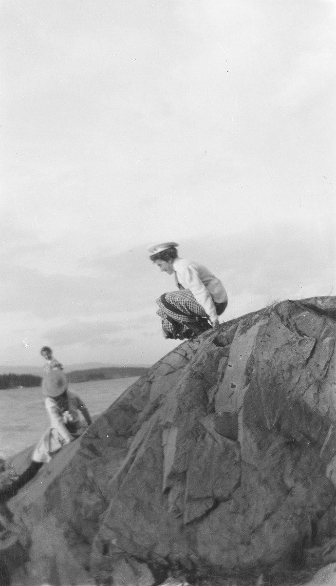 Celina Ihlen Mathiesen sitter på huk på et berg ved sjøen. Litt nedenfor ser vi døtrene Celina Marie og Ise (Louise) Mathiesen.