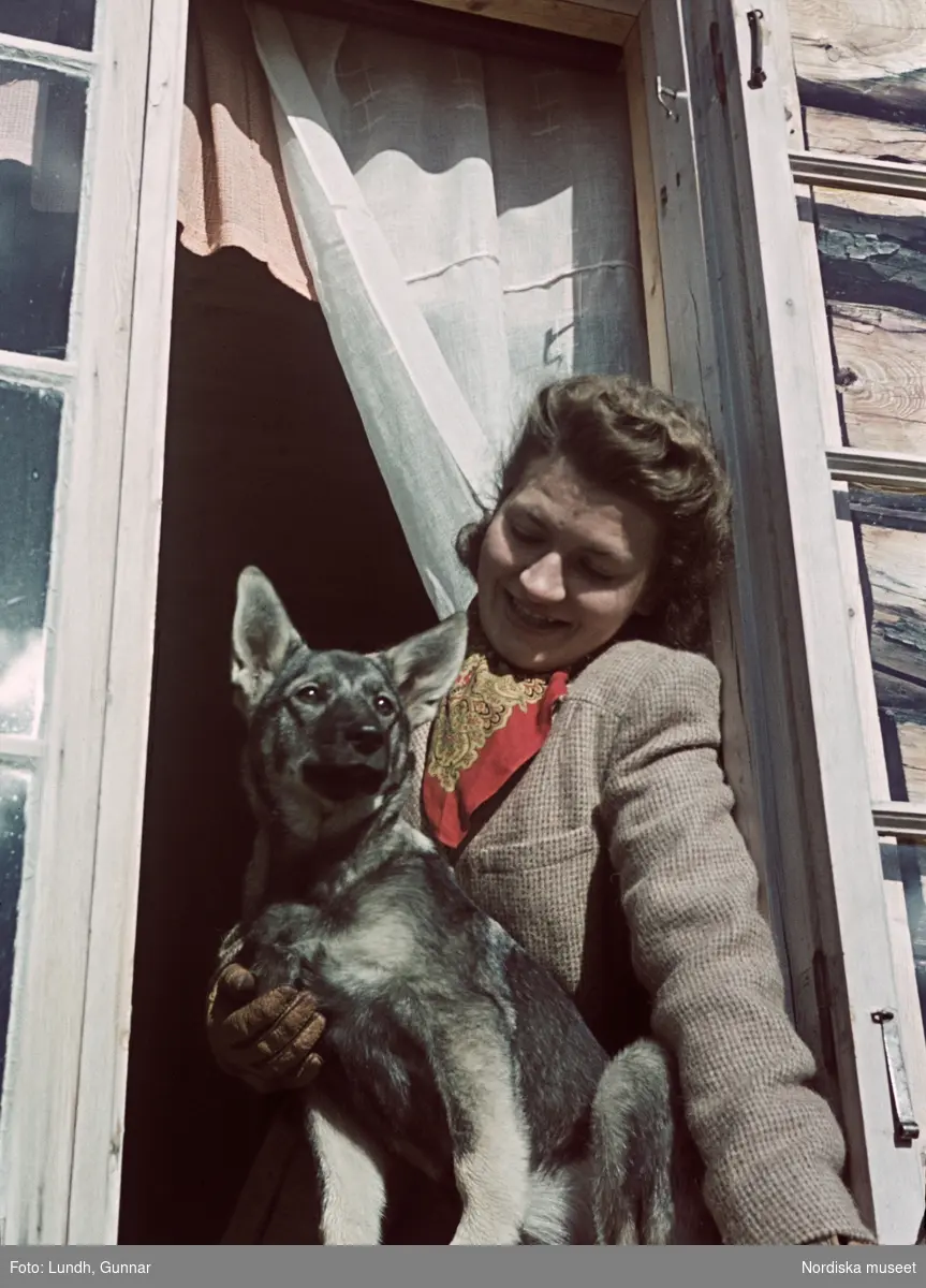 Kvinna i tweedkavaj sitter i ett fönster och blickar ned på en hund som sitter framför henne på fönsterbrädan.