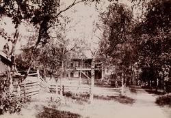 Et hus blant trær, på høyre siden en vei.