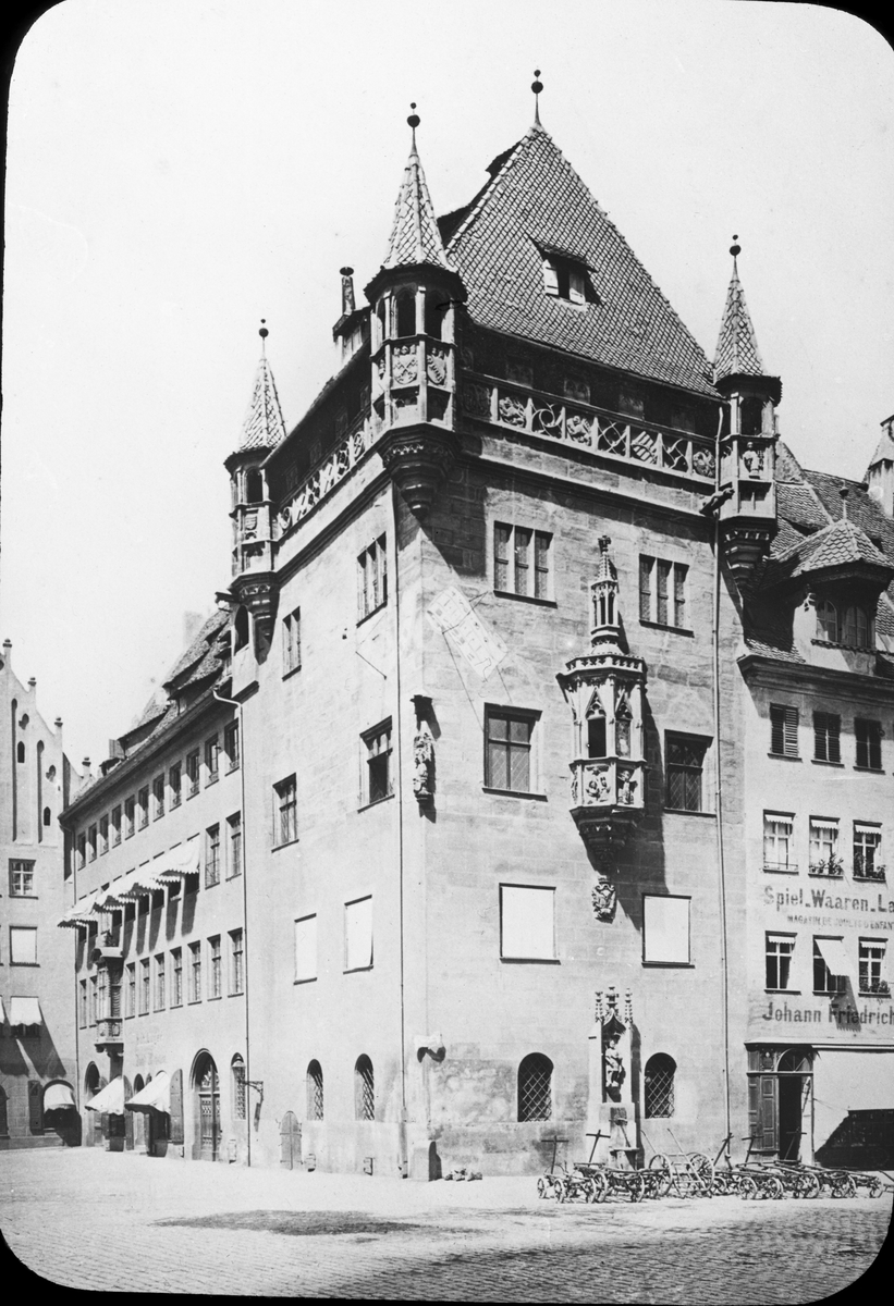 Skioptikonbild med motiv av hus från 1400-talet i Nürnberg. Medeltida hus av röd sandsten. 
Bilden har förvarats i kartong märkt: Nürnberg XII. 1901. Text på bild: "Das Nassauerhaus XIV talet".