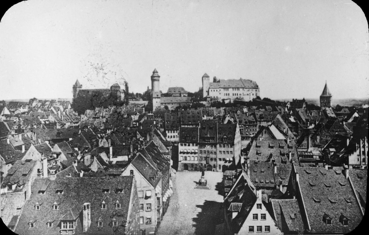 Skioptikonbild med motiv av vy över Nürnberg med Kaiserburg (Kejsarens Slott) i bakgrunden.
Bilden har förvarats i kartong märkt: Nürnberg XII.  1901