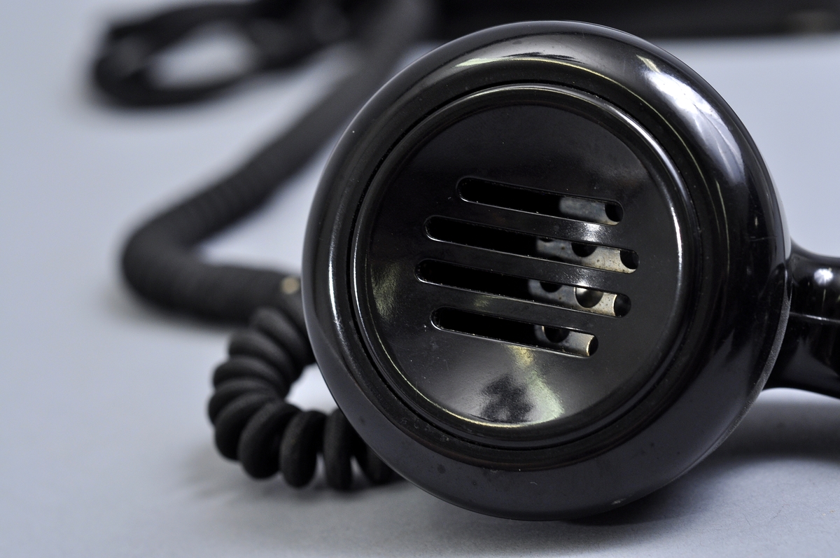 Telefonapparat BC 560, ändstationsapparat för AT-system. Bordtelefon modell m50 av svart bakelit med silverplåt och textilklätt apparatsnöre anslutet till väggplint utan lock.
