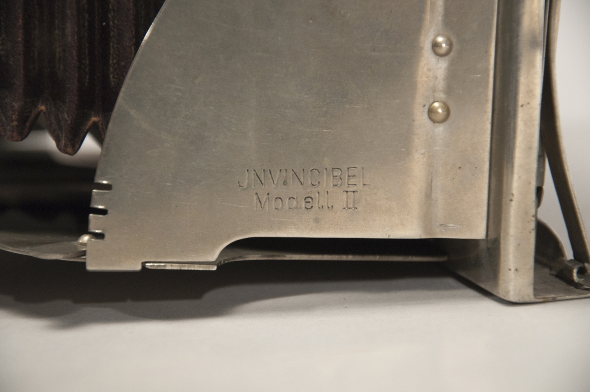 Hopfällbar bälgkamera enlig H. Maders patent.  
Märkt: JNVINCIBEL Modell II.
Olika märkningar på kameran: i stativfästet på undersidan "4", på slutarens baksida "7".