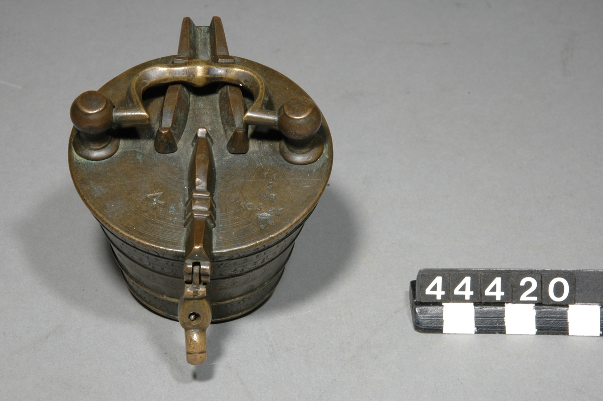 Insatsvikt av mässing, med dubbla balkar och låskläpp på locket, med handtag. Vikt 4 skålpund, 8 delar: 2 skålpund / 1 skålpund / 16 / 8 / 4 / 2 / 1 / 1/2 lod. 
Tillverkad av Johann Paulus Braun 1750, gälbgjutarmästare i Nürnberg. Märke: Man med träd.
Krönt av EH = Esaias Hackzell  1750-12-05.