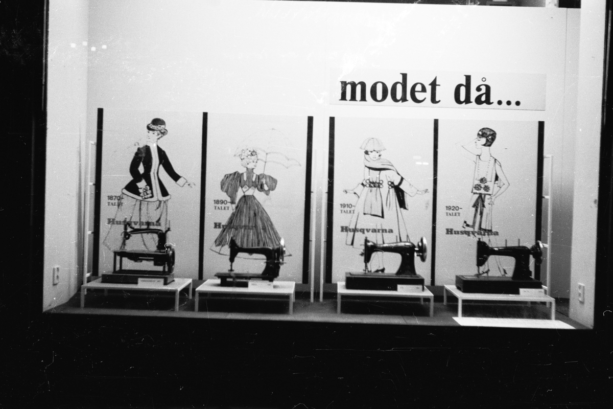 Ett skyltfönaster i Huskvarna med olika varianter på Husqvarna symaskiner och reklambilder på kvinnomodet 1870-1920 i bakgrunden.
