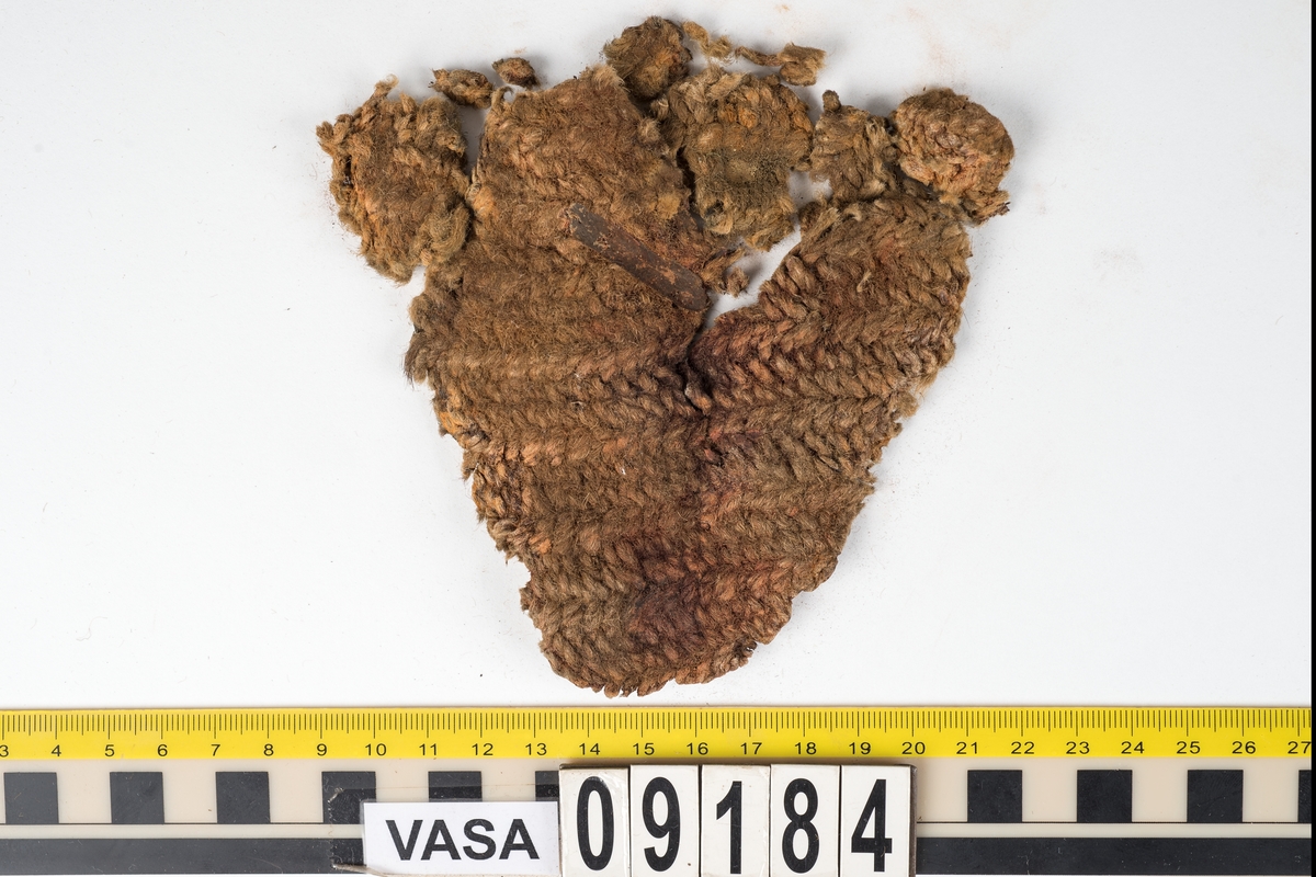 Penningpung.
2015 dokumenterades åtta textilfragment med fyndnummer 09184. Det är ett stort fragment samt sju små fragment som lossnat från det stora fragmentet. Fragmenten är nålbundna av ullgarn. 

Tidigare beskrivning: Penningpung av textil, utan botten.