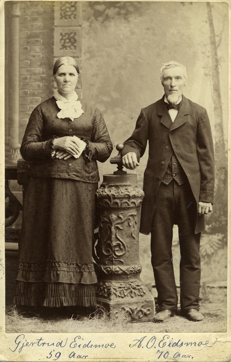 Portrett av en eldre kvinne og mann. Begge står i et studio og  begge er iført finklær.