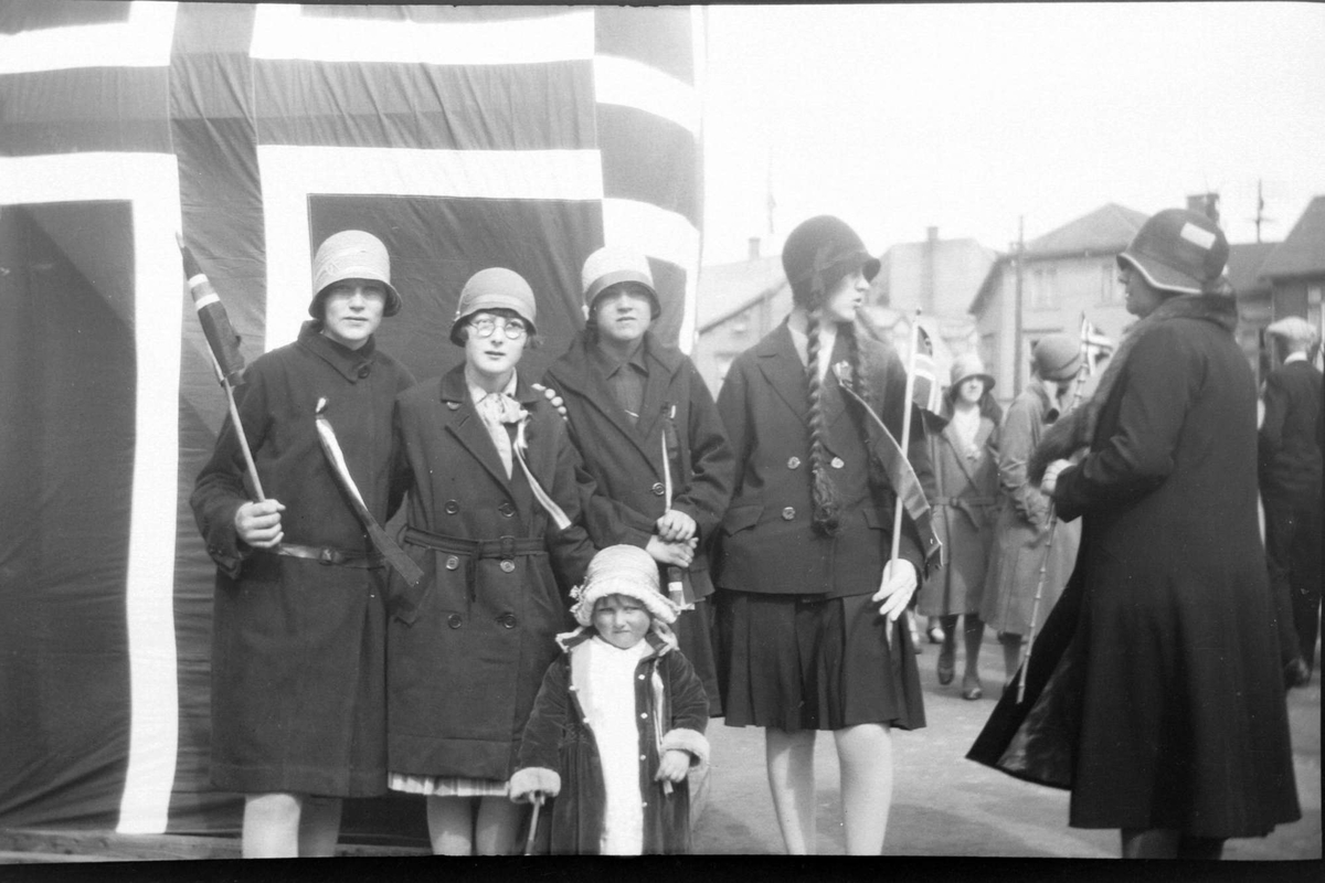 Fire 17. maikledte damer og ei lita jente, fotografert foran flagg.
