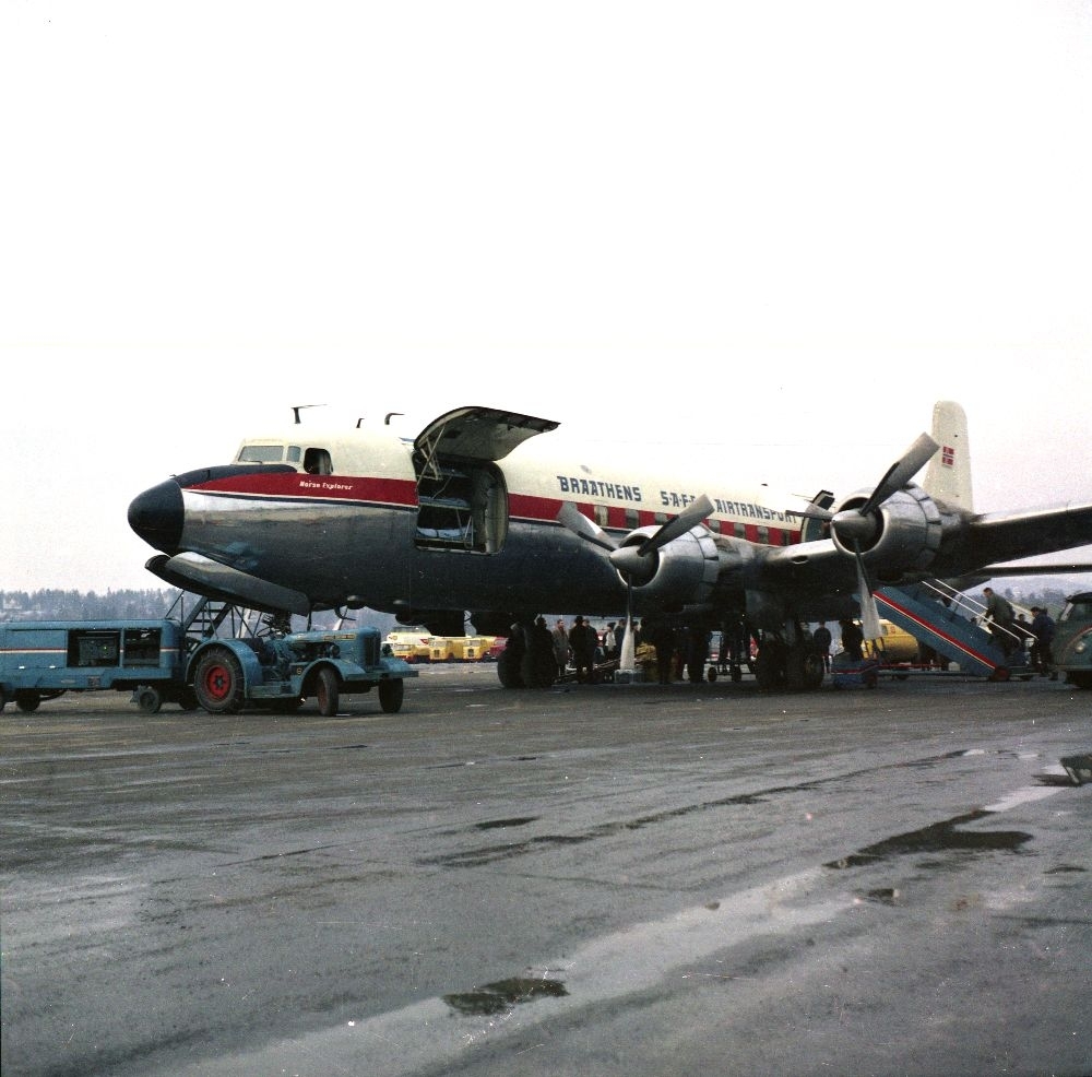 Lufthavn/Flyplass. Et fly, LN-SUI, DC-6A/C Liftmaster, fra Braathens SAFE, 
parkert. Passasjerer og last tas ombord.