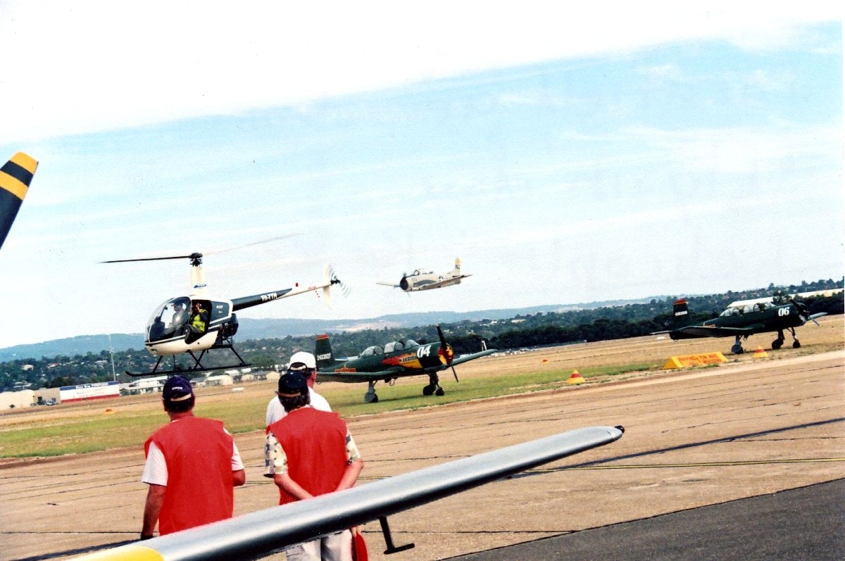 Et Robinson R22 helikopter, etterfulgt av en T-28 Trojan, som flyr oppvisning under et flystevne. To fly på bakken.