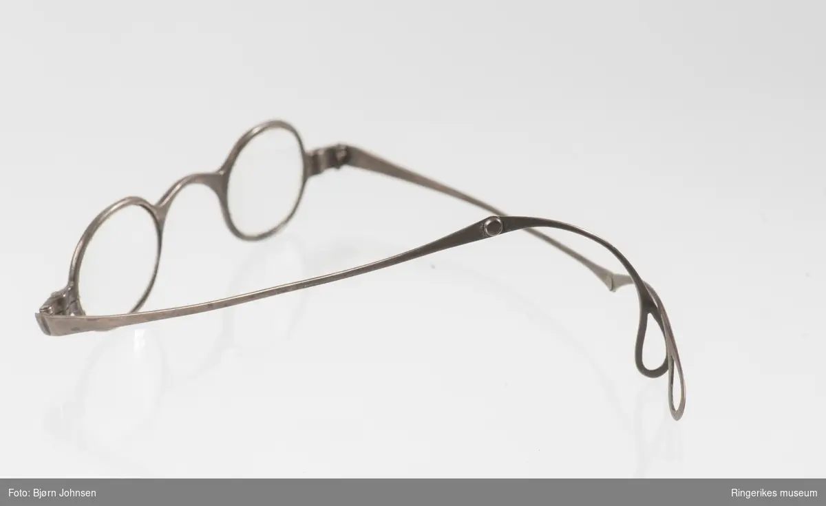 Leddet innfatning med to stenger som kan brettes sammen/ strekkes ut. Tilnærmet smal, oval utformet front med tilpasset brilleglass.