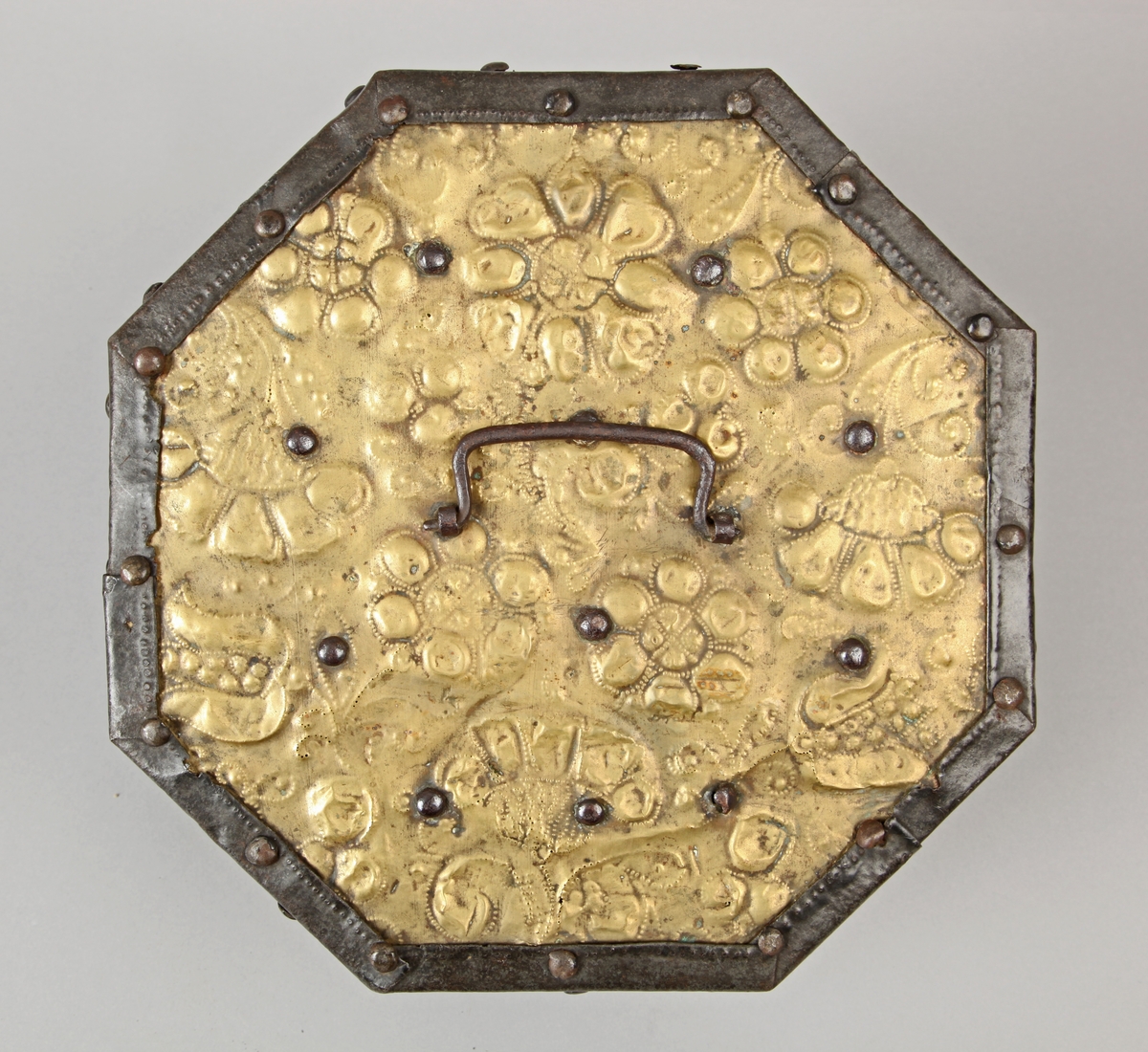 Åttekantet. Den har dekorerte flater i messing med jernbeslag og det hele er naglet på tre. På lokket er det en hank. Flaskefôret er låsbart, men den originale nøkkel mangler.