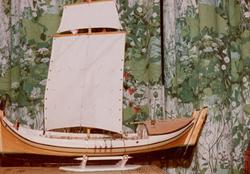 Modell av nordlandsbåt, fotografert med 70-tallsgardiner i b
