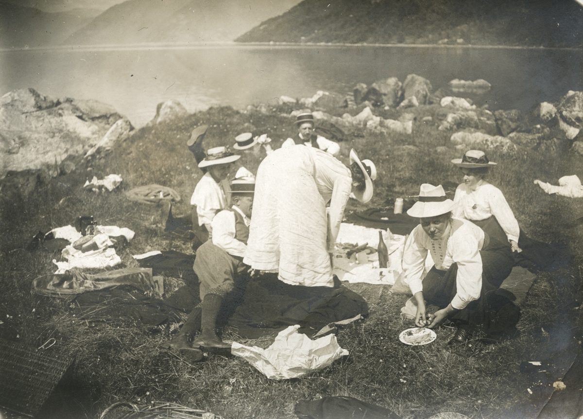 Menn og kvinner på picknick ved ein fjord.
