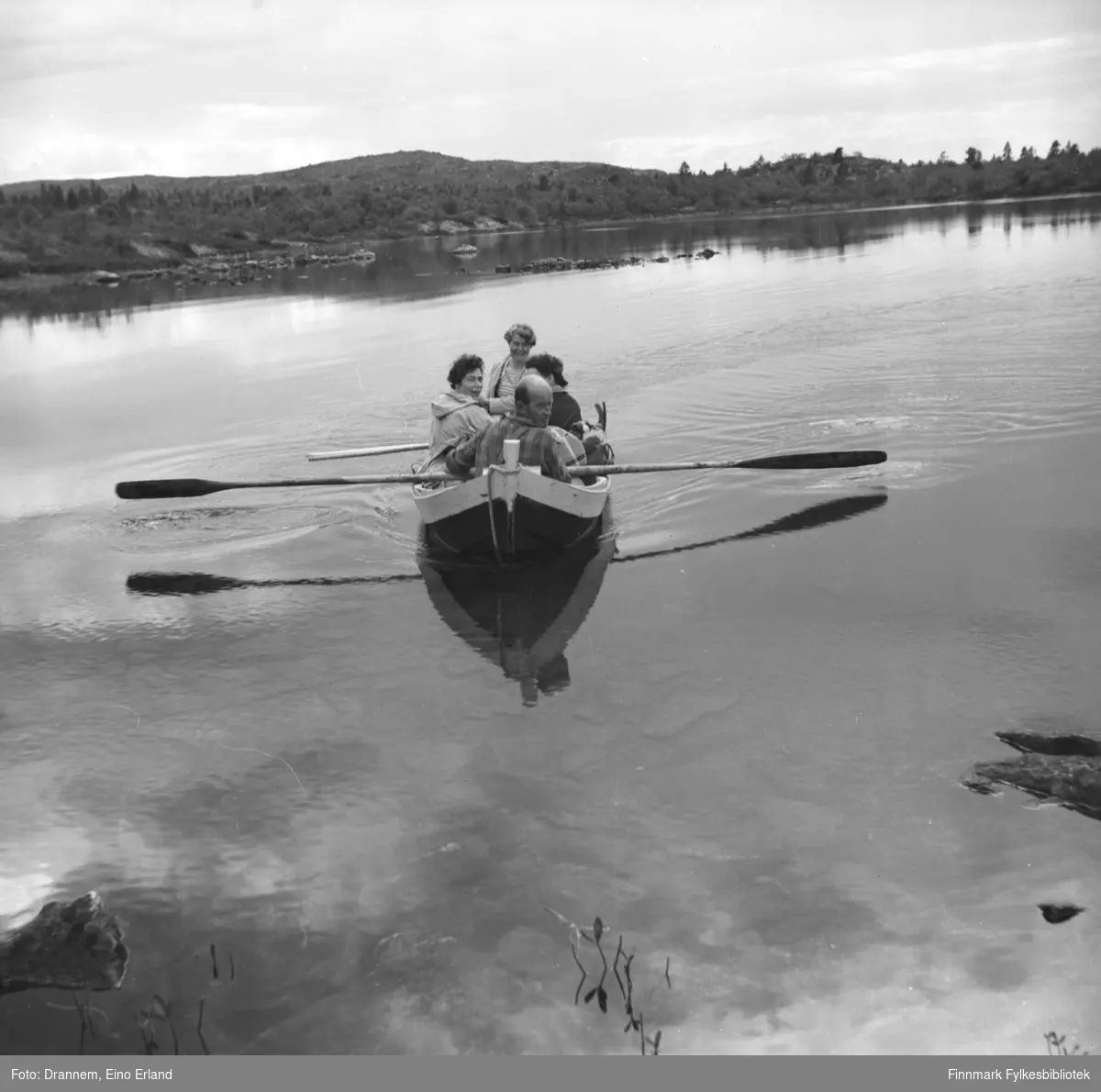 Fire personer sitter i en robåt. Jenny til venstre, Sonja bak og Uuno foran. En ukjent dame ses til høyre i båten.