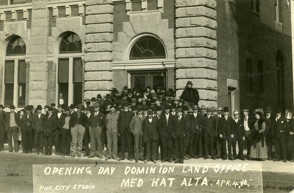 Postkort sendt fra Canada 3. oktober 1910. Bildet viser nybyggere foran Dominion land office. Blandt dem er Gilbert Bymoen