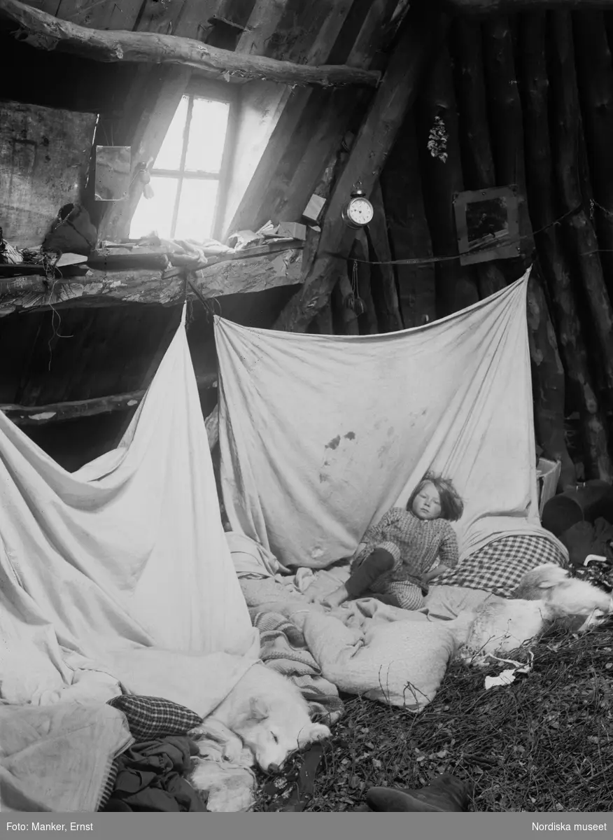 Interiör från Olof Andersson Ommas kåta i Strimasund. Morgonscen med rakkas och sängkläder. Ett barn och en hund ligger och sover.
