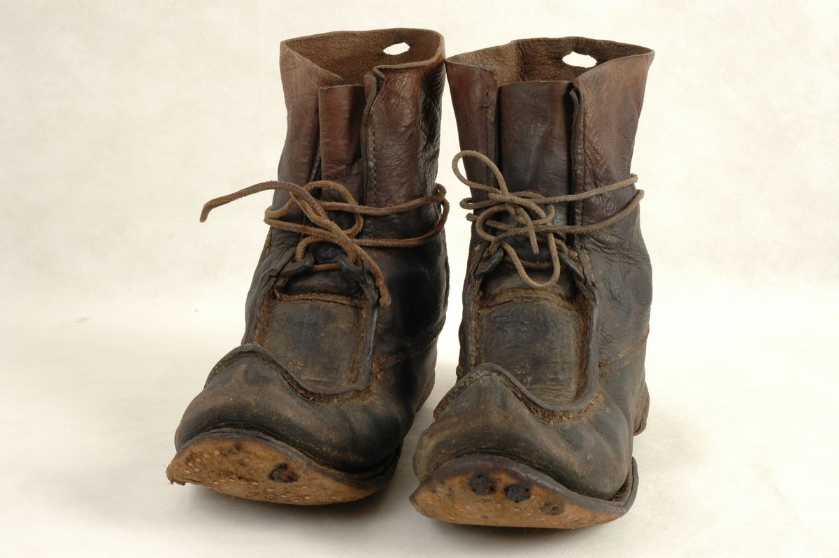 Et par sko av samisk type. Alt i lær. Skinnreimer til knytting rundt ankel. Liten dekor preget inn i læret på oversiden av skoen og bokstavene F L.