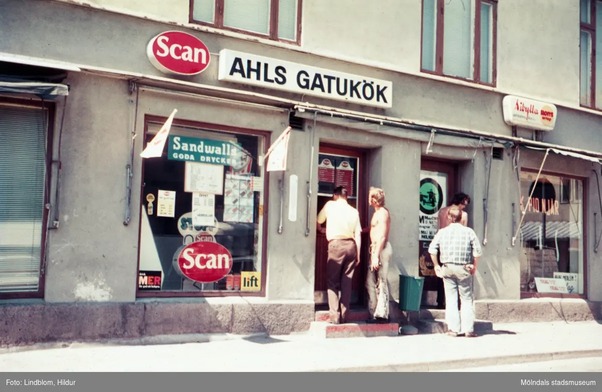 Fyra män står utanför dörren till Ahls Gatukök vid Gamla Torget i Mölndal med adress Kvarnbygatan 43, 1970-tal.

För mer information om bilden se under tilläggsinformation.