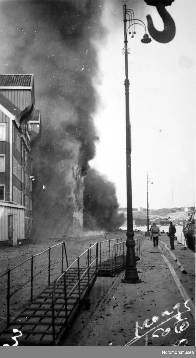 Andre verdenskrig har kommet til Kirkelandet i Kristiansund. Her ser vi det brenner ved Smithbrygga på Storkaia. Bildet er datert 28. april 1940, som er samme dag som byen ble bombet for første gang. langanger. Fra Nordmøre museums fotosamlinger. dublett