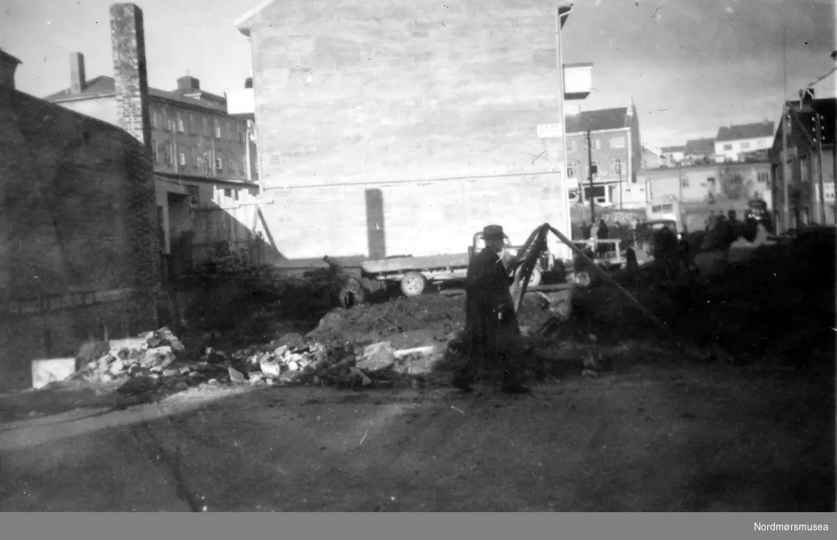 På bildet ser vi tomten etter Slakter Løvolds forretning, etter at restene av hans hus fra brannen i 1940 er blitt fjernet (se 1029). I bakgrunnen ser vi murgavlen til Neergaards hus i Nedre Enggate. Til venstre ser vi brakker ved den høgre skole. Til høyre ser vi oppover Nedre Enggate, samt litt av den gamle Hvedingbrakken. Bildet er datert desember 1949. Fra Nordmøre Museums fotosamlinger.