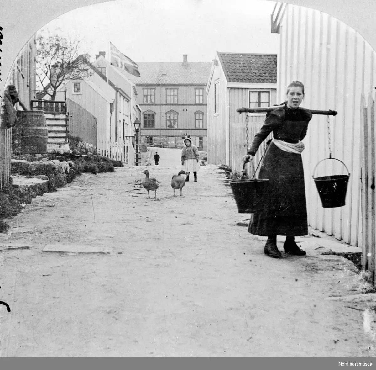En kvinne med børtre i en bygate. 
 Fra Nordmøre Museum sin fotosamling
