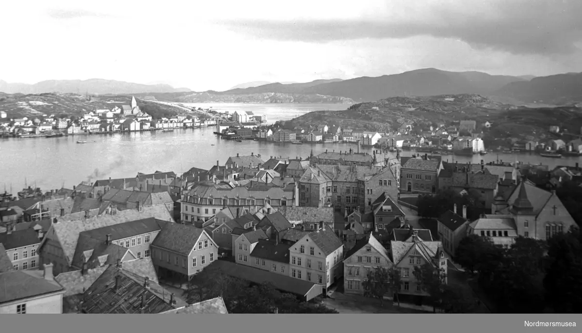 På bildet ser vi de 3 øyene med bebyggelse som utgjør en del av Kristiansund, med Kirkelandet midt på bildet nærmest, Nordlandet til venstre hjørne og Innlandet til høyre. Bebyggelsen er fra før bybrannen den 28. april 1940, da tyskerne bombet byen. Skoleplana foran, bedehuset til høyre. Fra Nordmøre Museum si fotosamling.